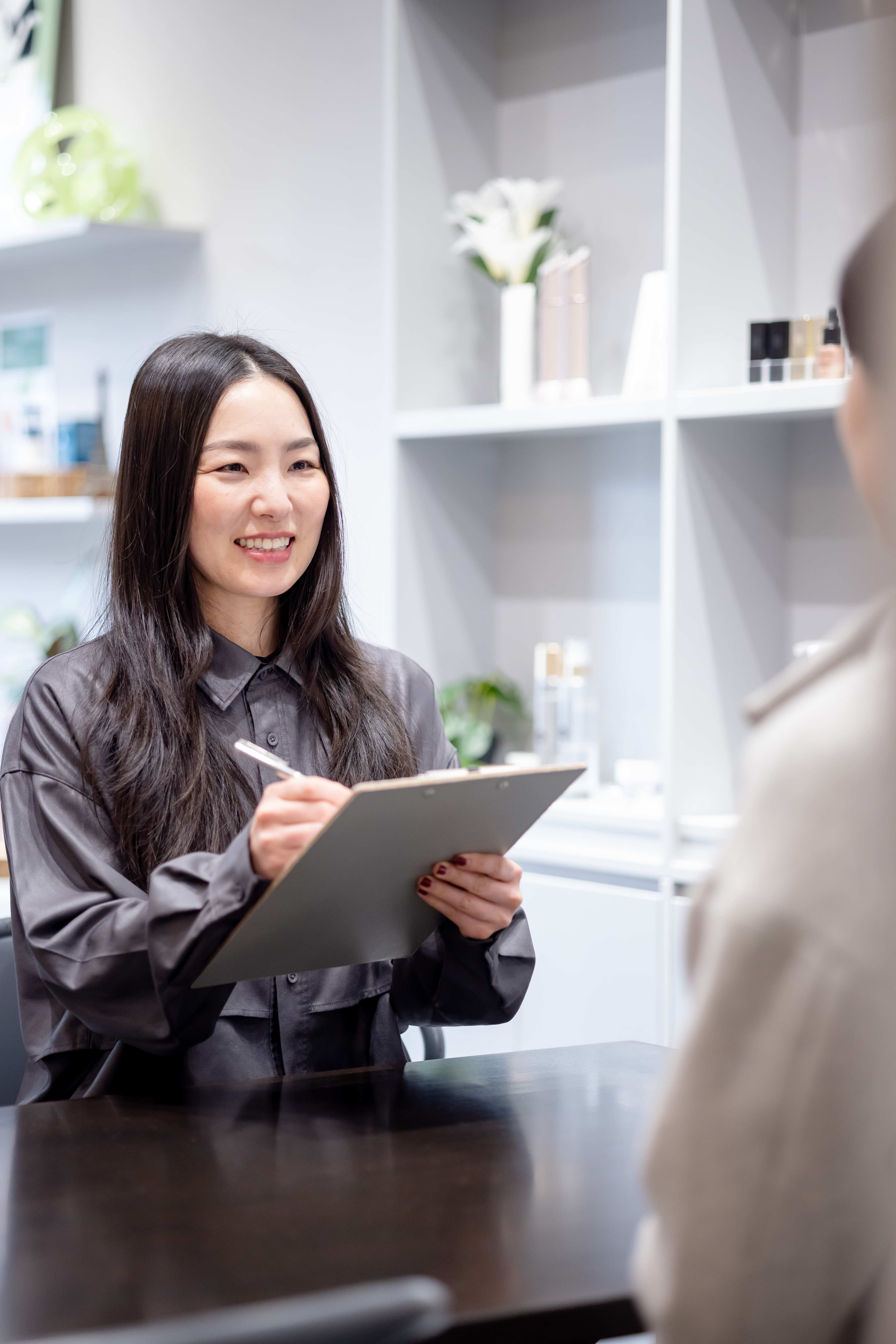 クリップボードを持ったスタッフが笑顔でお客様の状態を記録しながらカウンセリングしている様子
