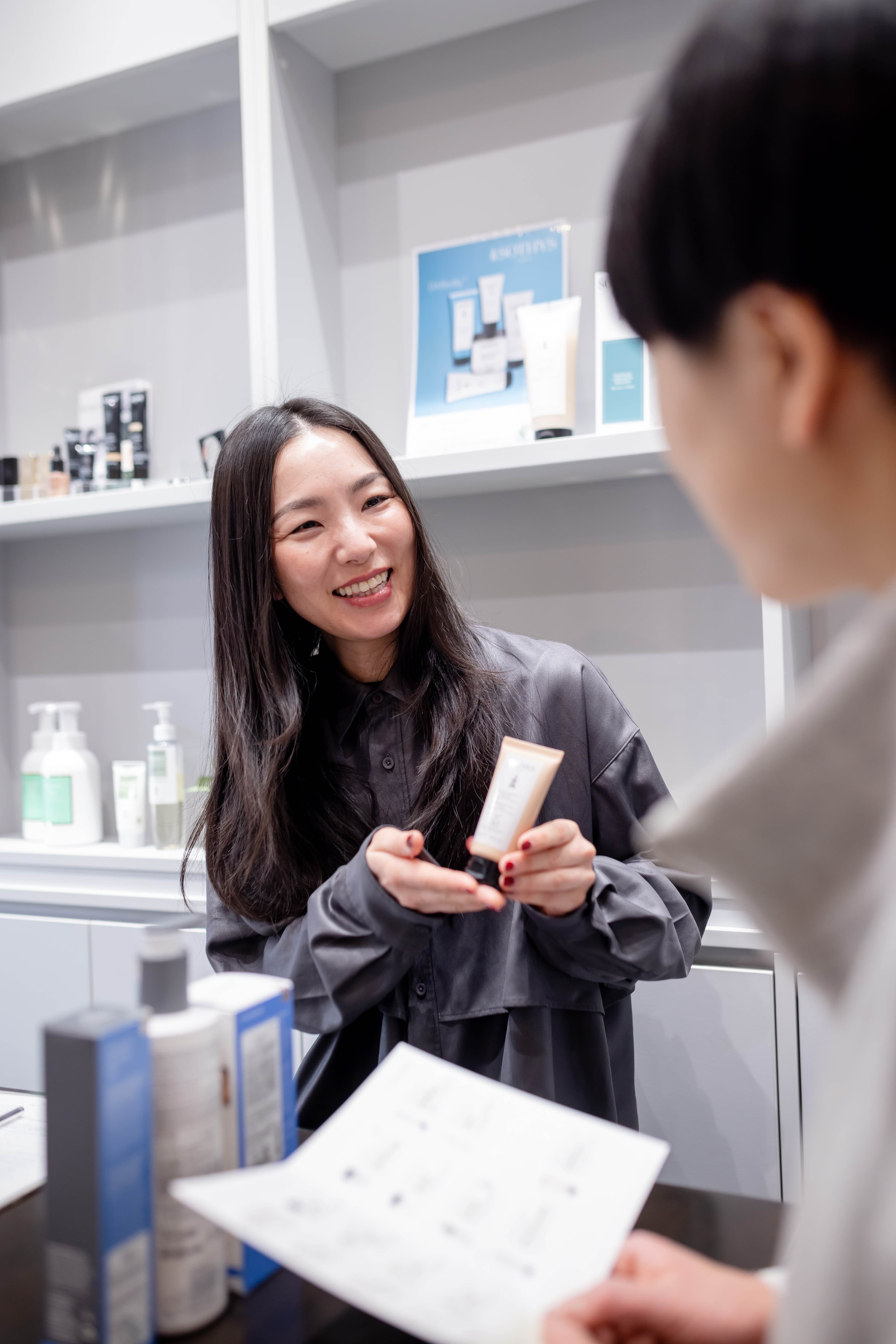 スタッフが笑顔でスキンケア製品を手に持ち、お客様に製品の使い方や効果を丁寧に説明している様子