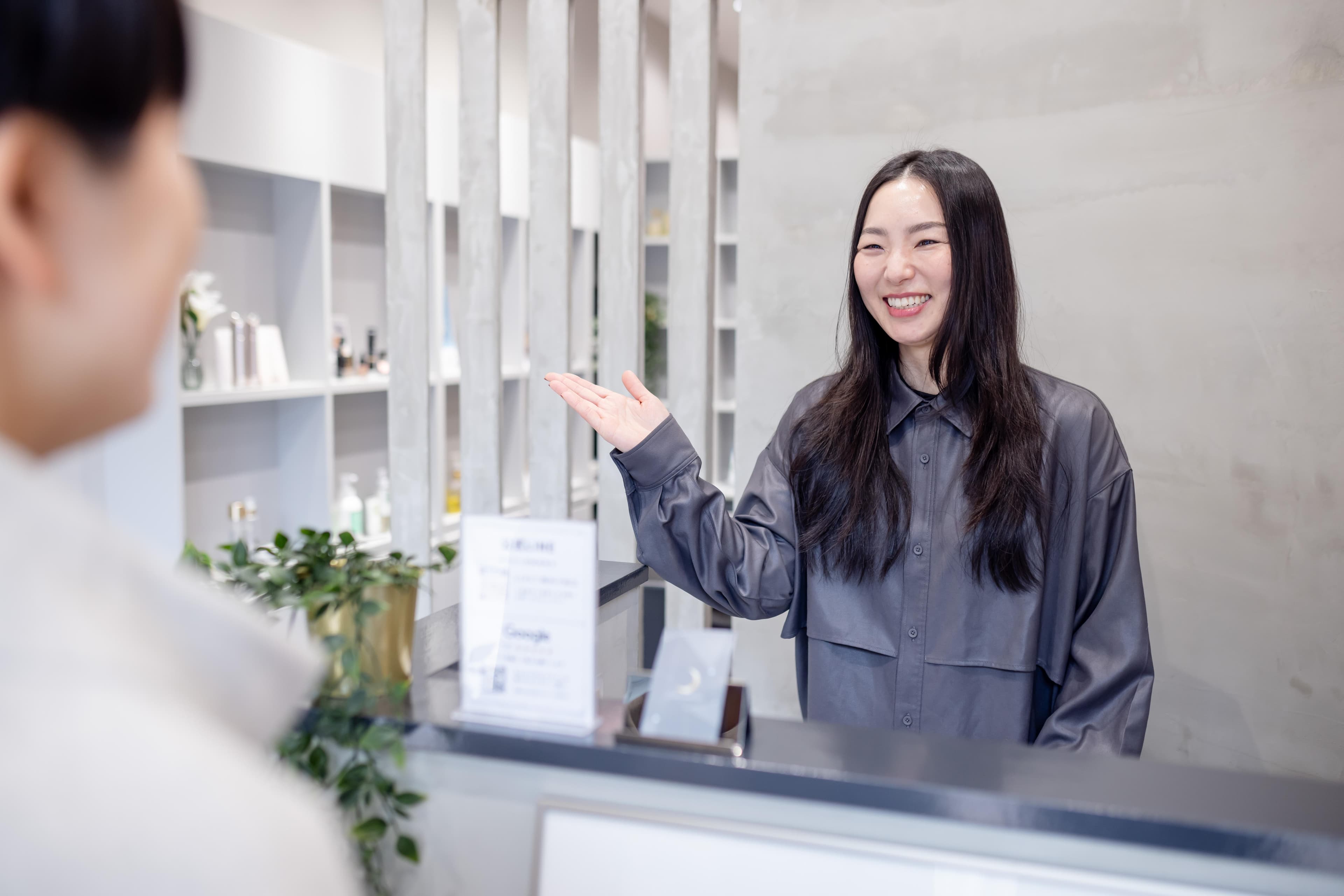 スタッフが店内の製品棚を背景に手を広げて、お客様に最適な商品ラインナップをご案内している様子